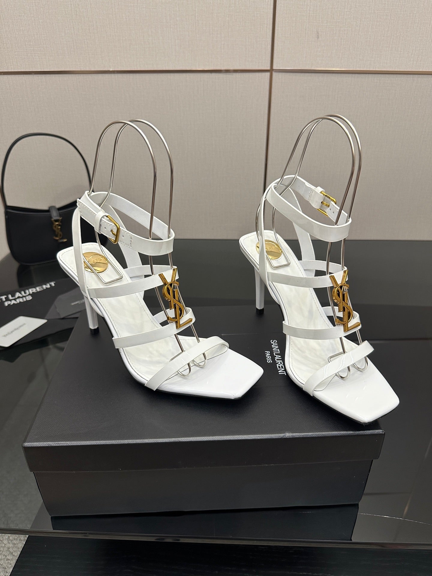 Pair of white high-heel sandals with gold-tone charms and open-toe, crisscross straps.