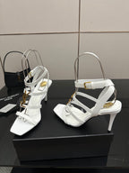 White high-heel sandals with wide strap across the foot and gold-tone hardware, side view.