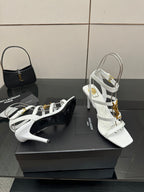 White high-heel strappy sandals with gold-tone buckles, shown from side angle.