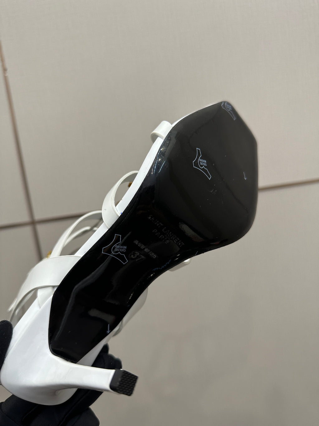 Black underside of a white high-heel sandal sole, showing brand markings.