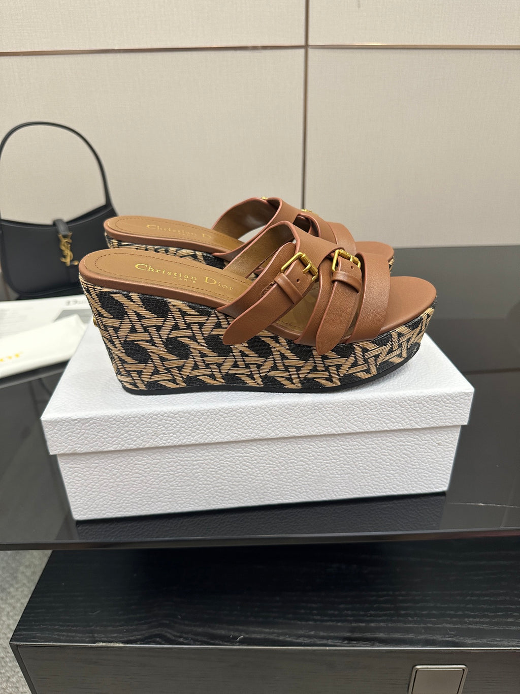 Tan leather wedge sandals with twin straps and gold buckles over patterned platform.