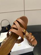 Tan leather slide sandal close-up with crisscross straps, gold buckles, and patterned footbed.