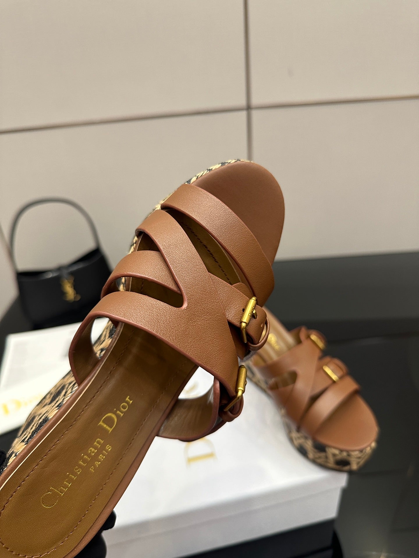 Tan leather slide sandal close-up with crisscross straps, gold buckles, and patterned footbed.