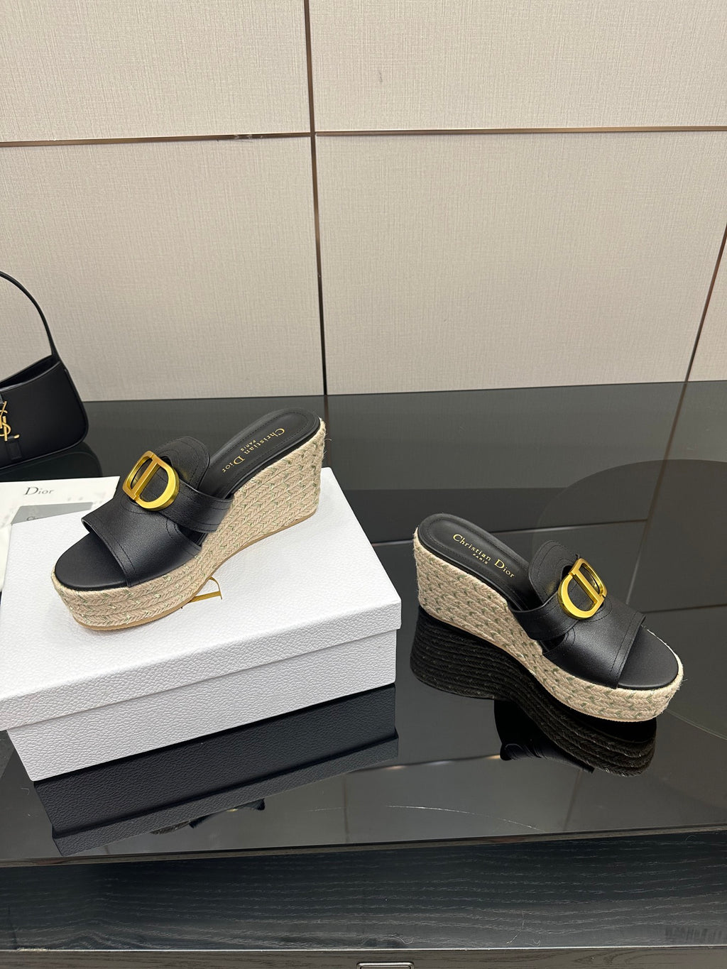 Black wedge mules with gold logo buckle and jute platform, side view.