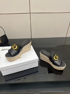 Black wedge mules with gold logo buckle and jute platform, side view.
