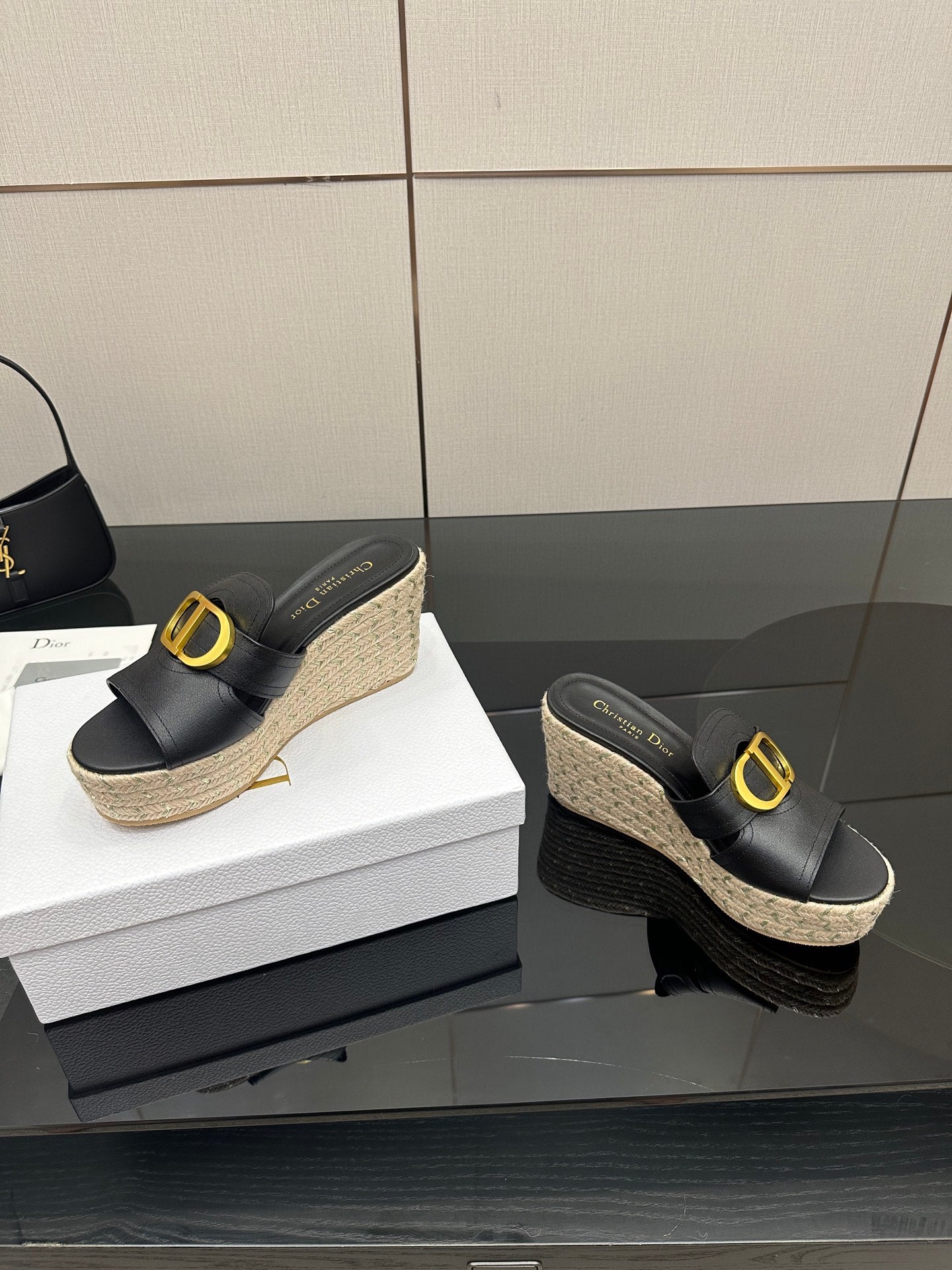 Black wedge mules with gold logo buckle and jute platform, side view.
