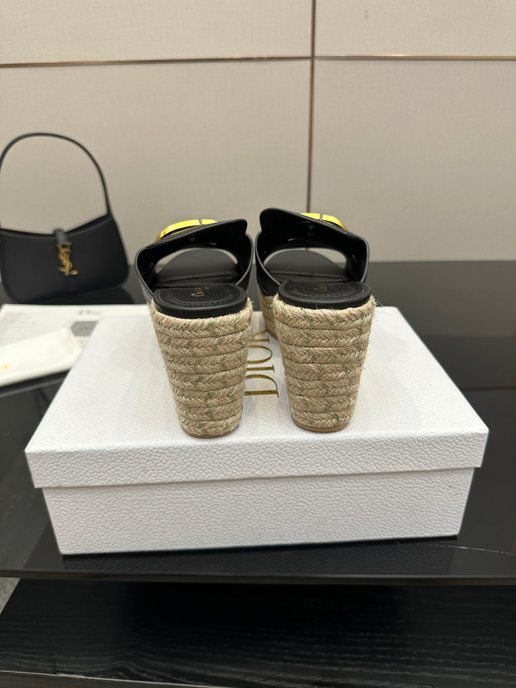 Pair of black backless wedge sandals with jute heels and gold logo buckle.