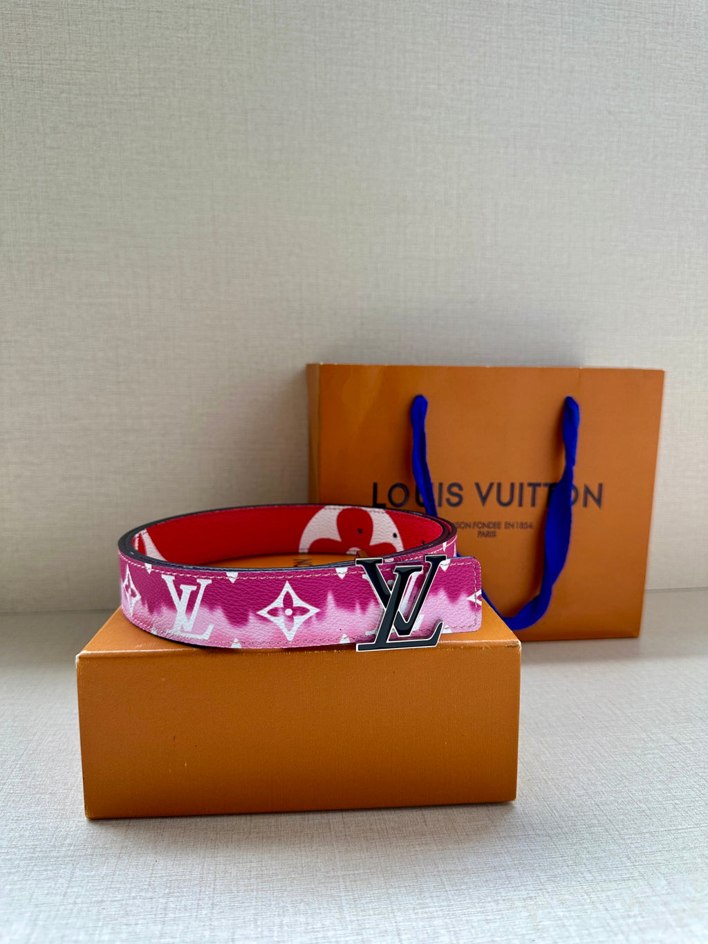 Louis Vuitton belt with pink monogram strap and LV buckle, laid on box.
