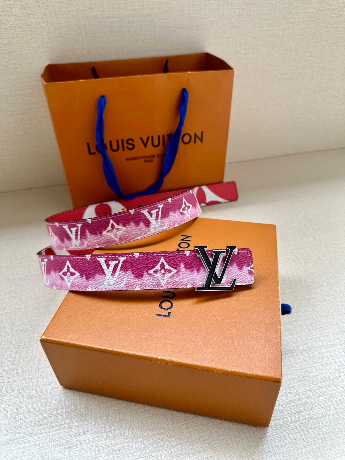 Louis Vuitton belt on a box, showing pink monogram strap and LV buckle.