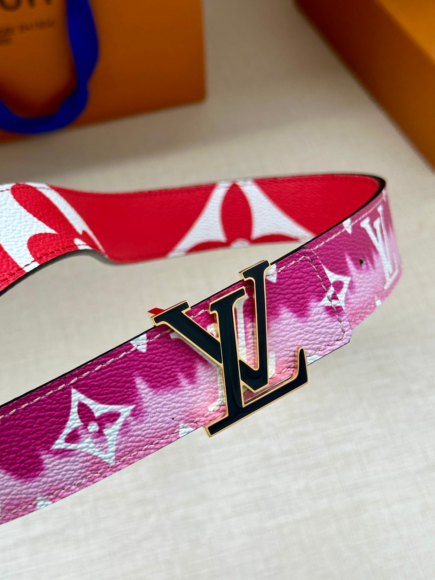 Louis Vuitton belt close-up with pink monogram strap and LV metal buckle.