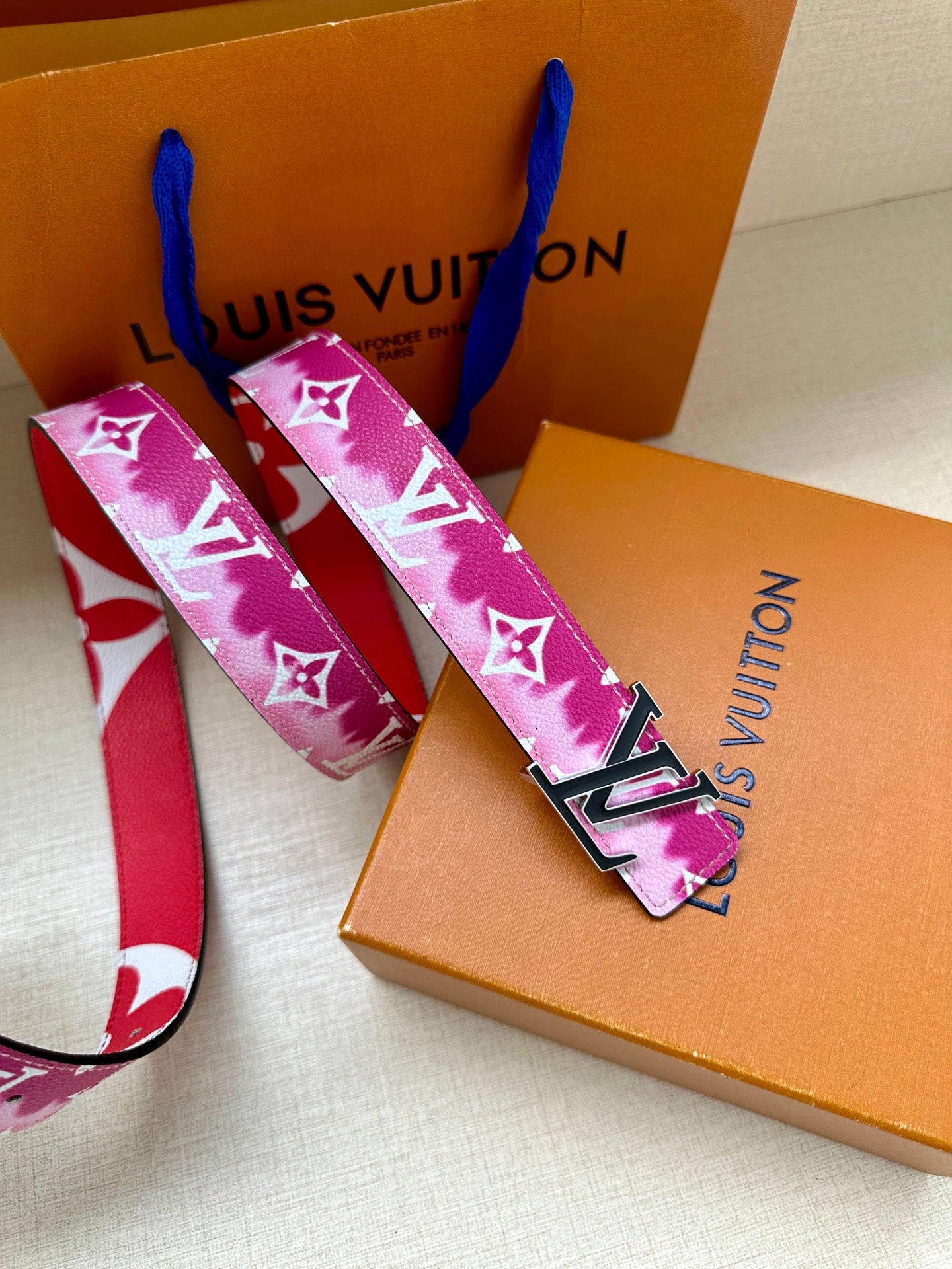 Louis Vuitton belt with pink monogram strap and gold-tone buckle on box.