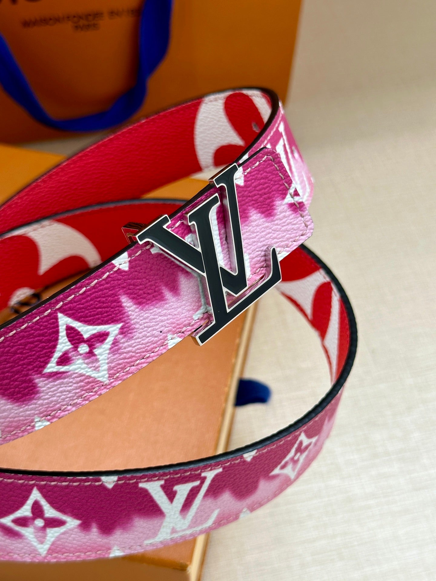 Louis Vuitton belt detail with pink monogram strap and metal LV buckle.