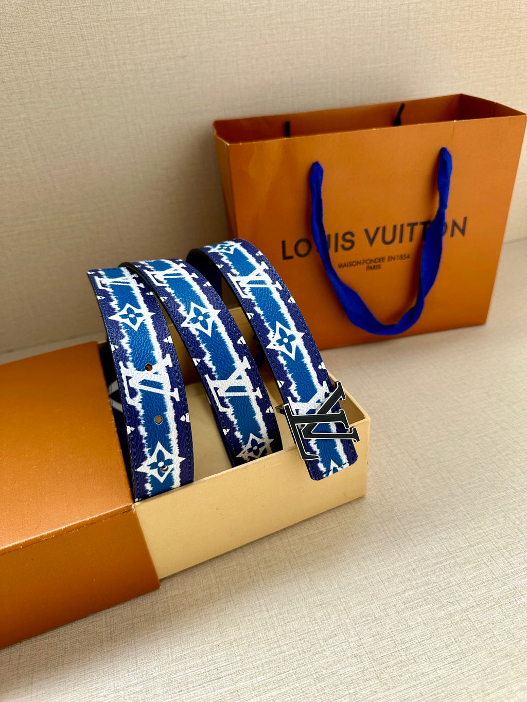 Blue and white monogram belt with gold buckle, shown on packaging
