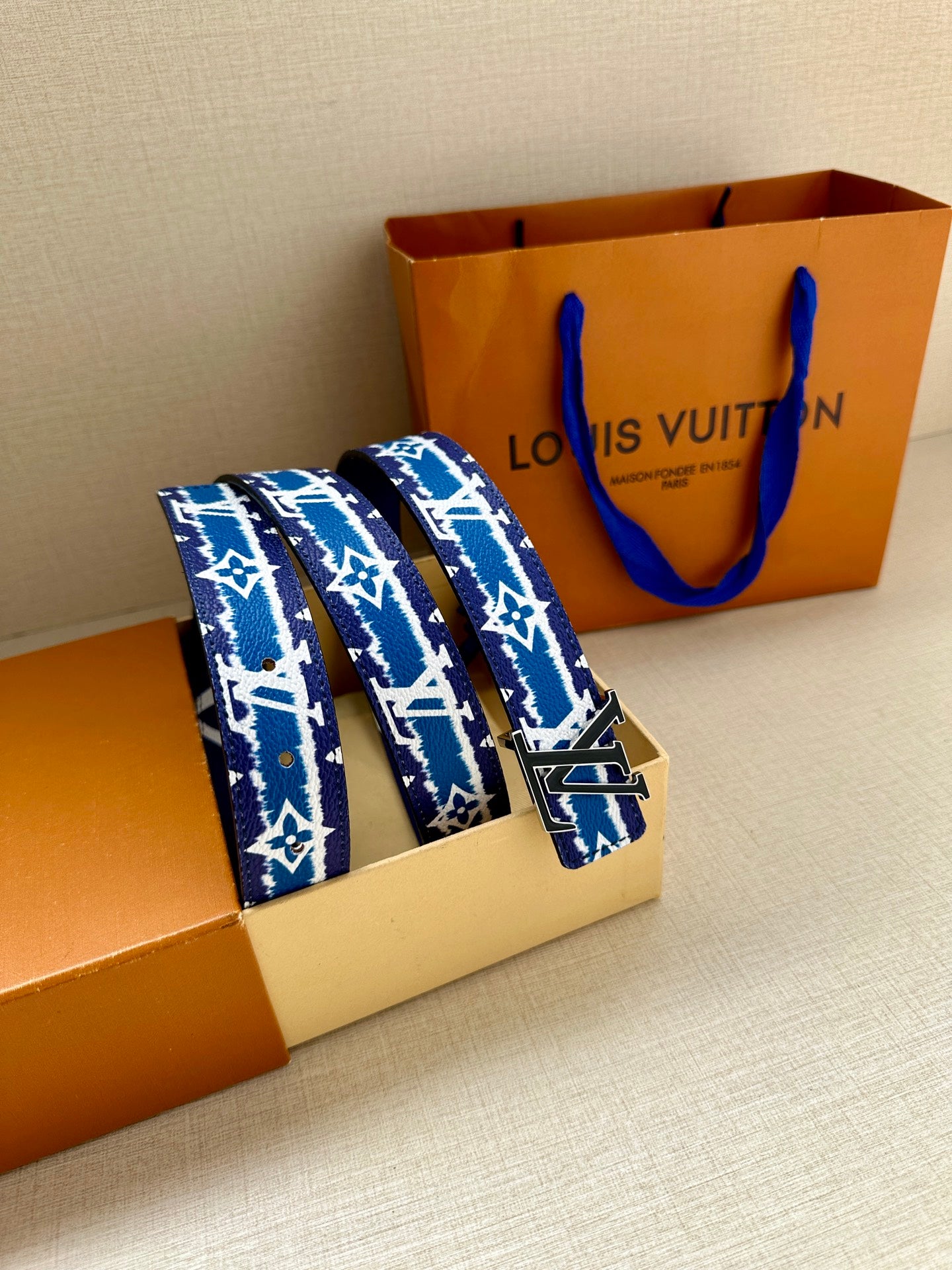 Blue and white monogram belt with gold buckle, shown on packaging