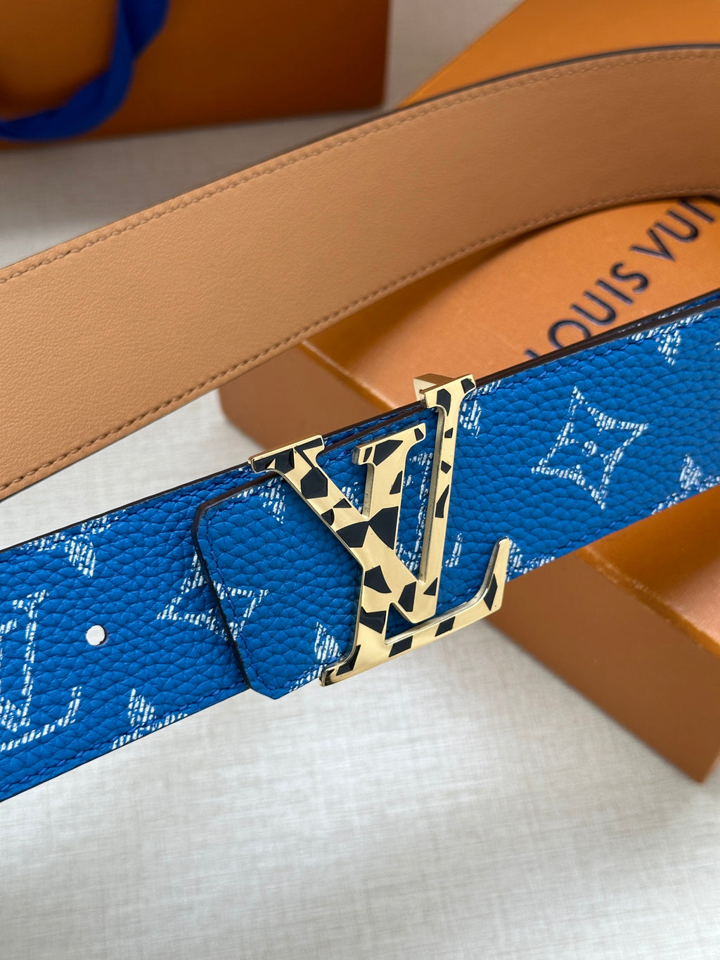 Blue logo-pattern belt detail with gold buckle and tan leather strap backing