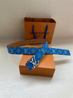 Blue monogram belt with gold buckle, shown across orange boxes and white base