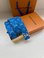 Blue monogram belt with gold-tone buckle and stacked strap ends on gift boxes
