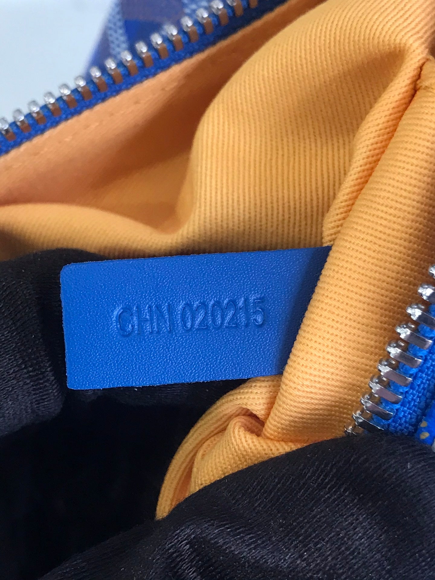 Blue fabric label with code stitching inside Goyard-pattern bag.