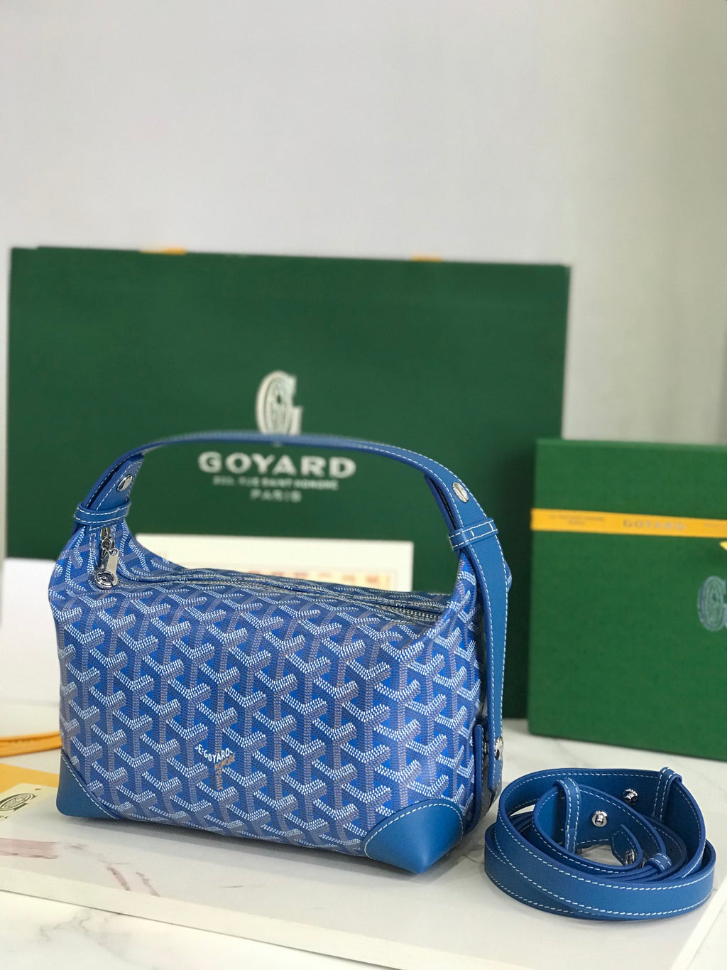 Blue Goyard-pattern hobo bag with top handle, gold zipper, leather trim.