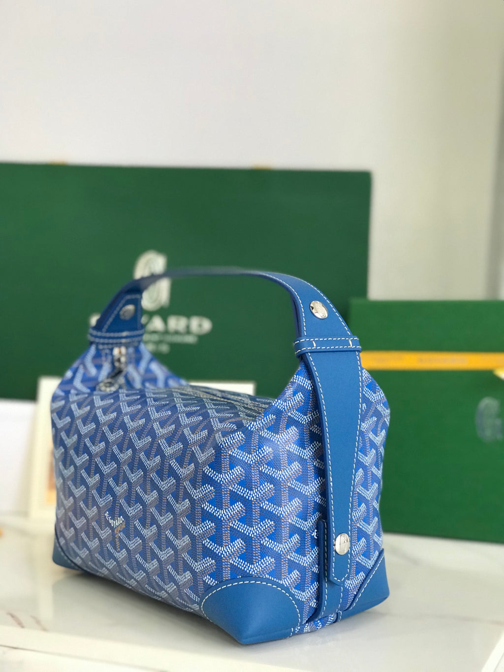 Blue Goyard-pattern satchel bag with side handles and textured leather bottom.
