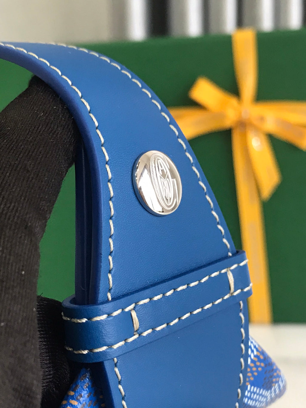 Blue leather corner with metal logo hardware and white-stitched trim on bag.