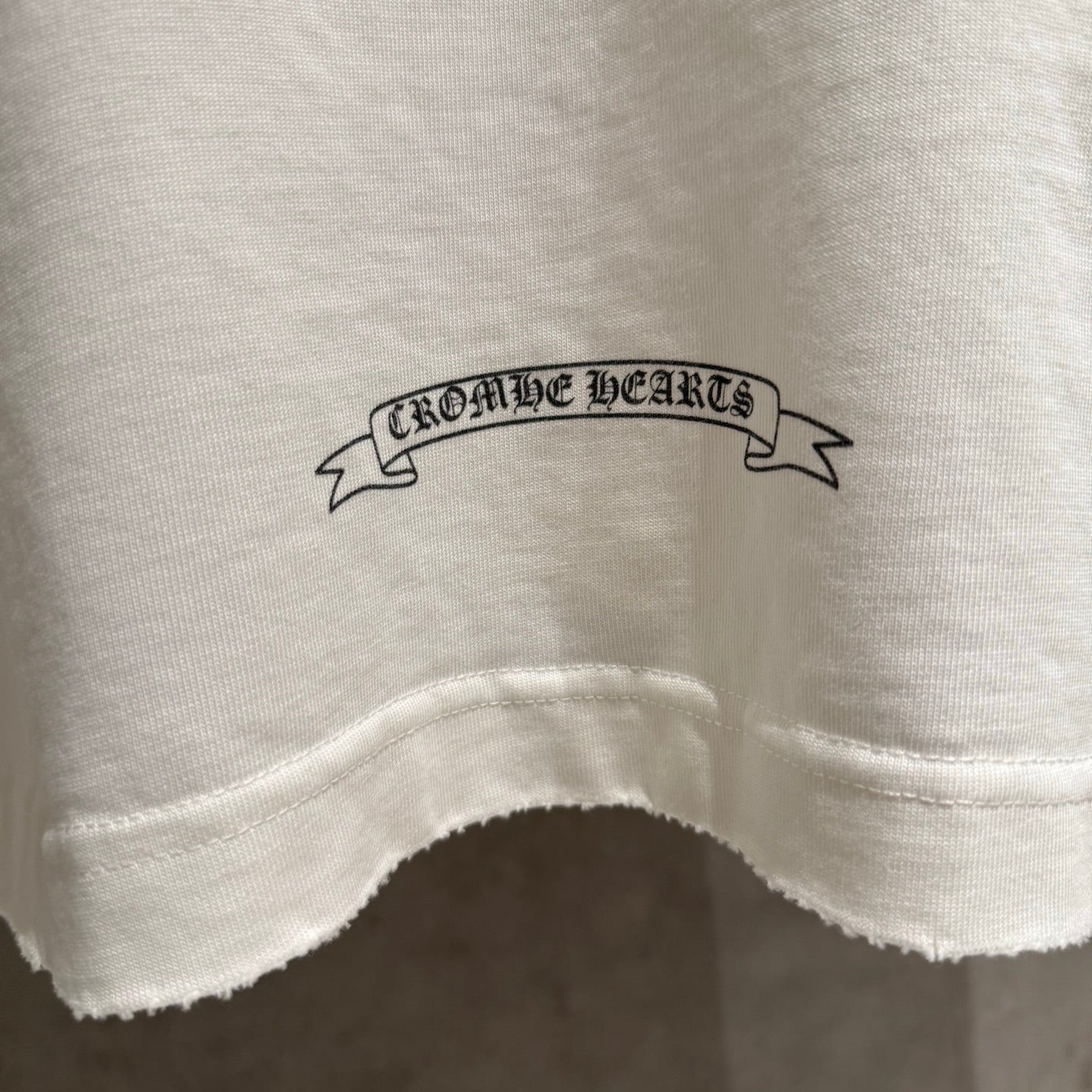 White long-sleeve shirt hem area with small printed ribbon text