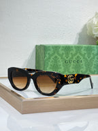 Gucci sunglasses, dark tortoiseshell frames with brown lenses and gold GG logo.