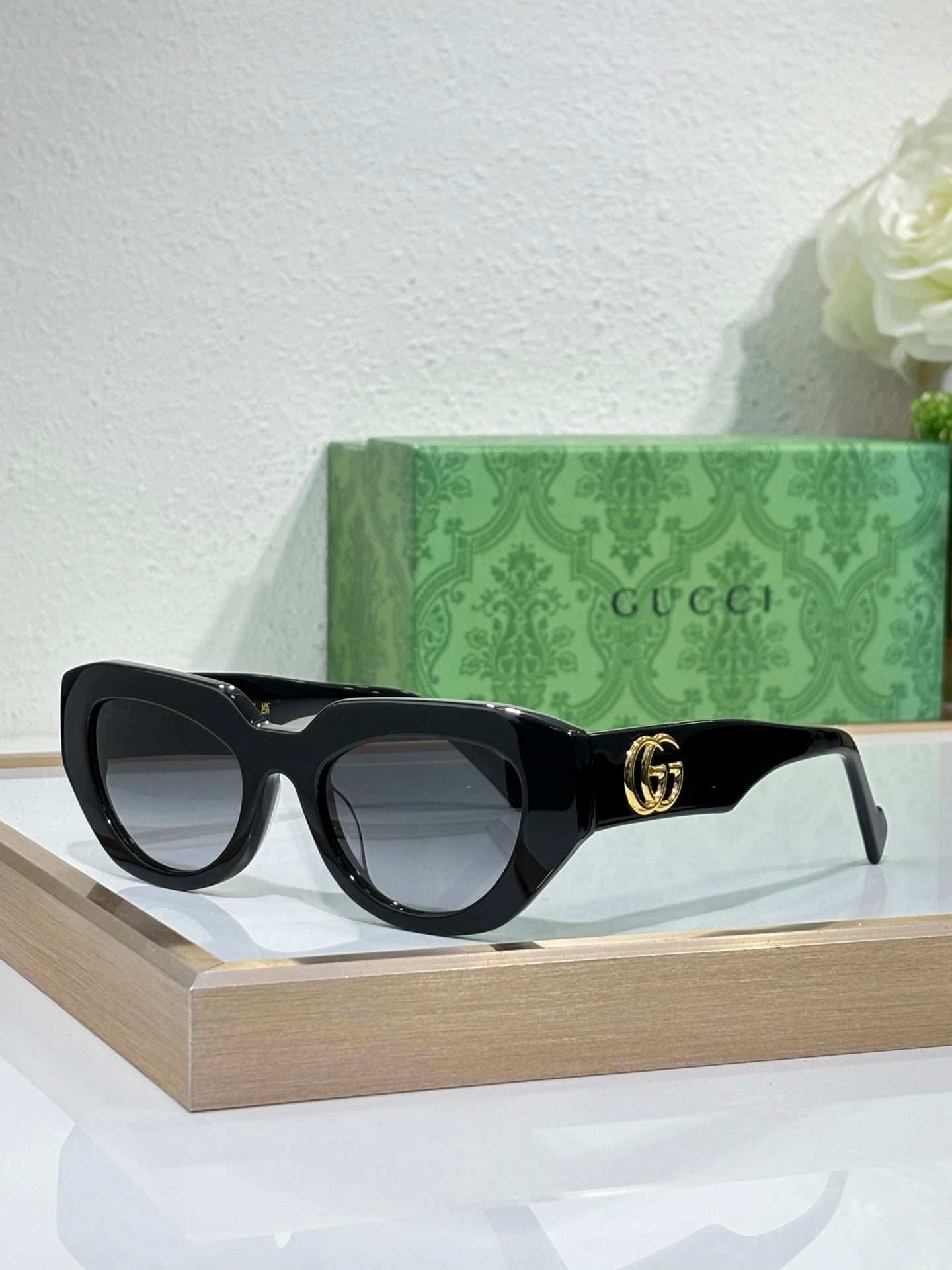 Gucci sunglasses, black frames with grey lenses and gold GG logo on temple.