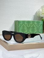 Gucci sunglasses, black frames with brown lenses and gold GG logo at temple.
