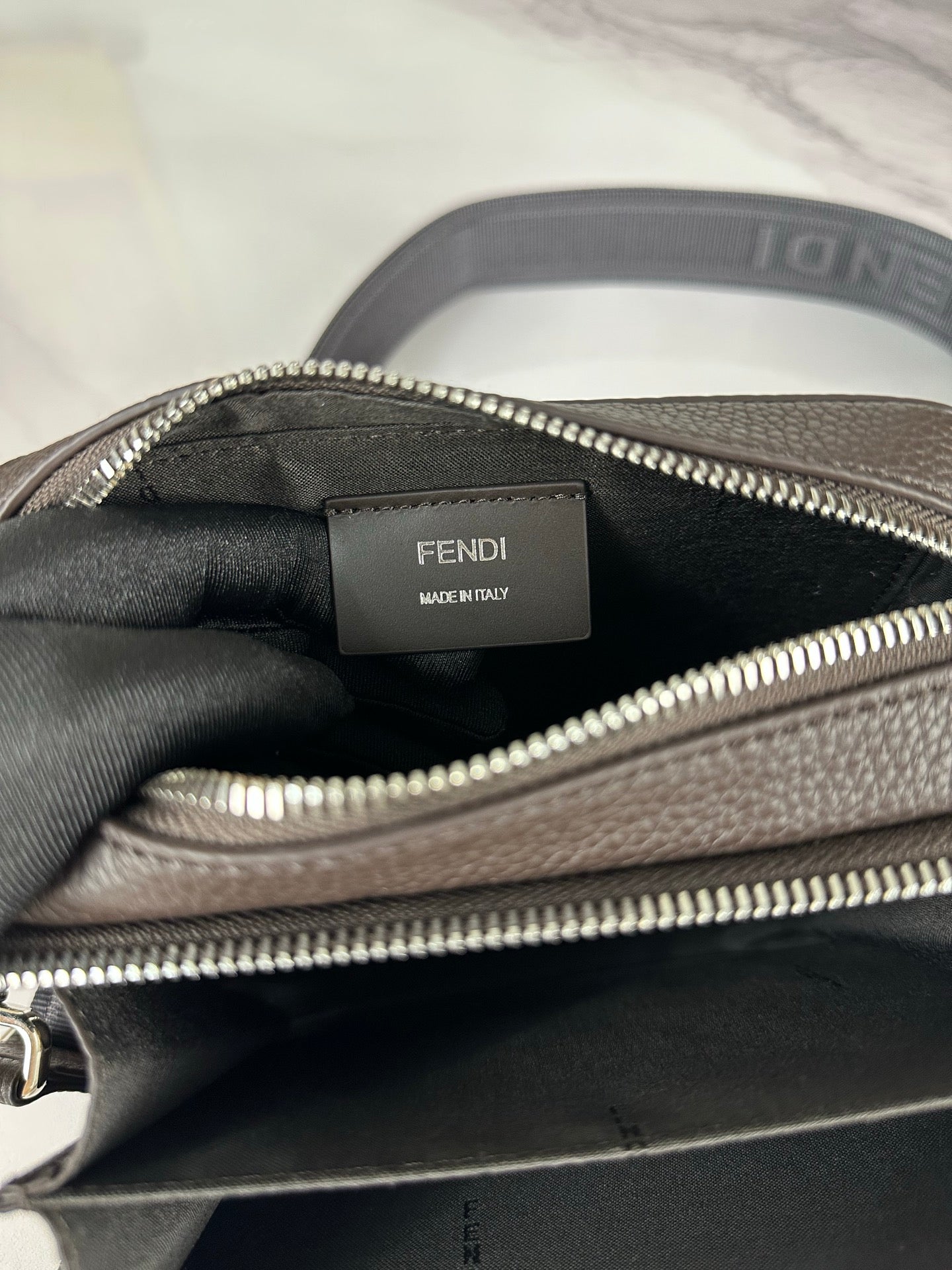 Fendi crossbody bag interior label and silver zipper trim with dark fabric lining.