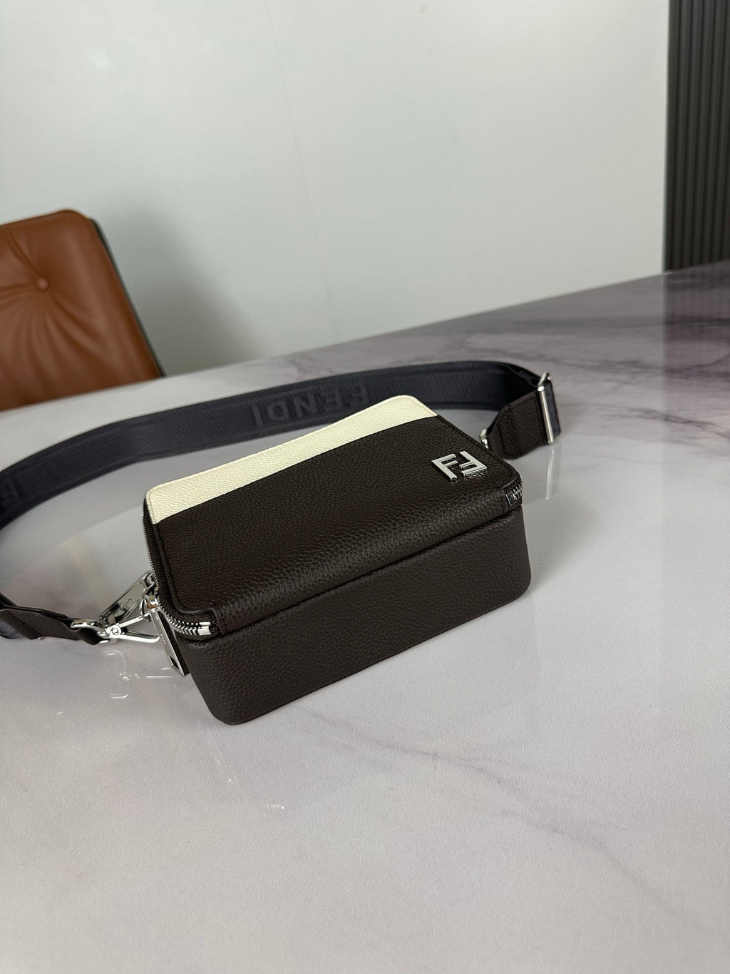 Fendi crossbody bag angled view with dark body, cream panel, and FENDI logo strap.