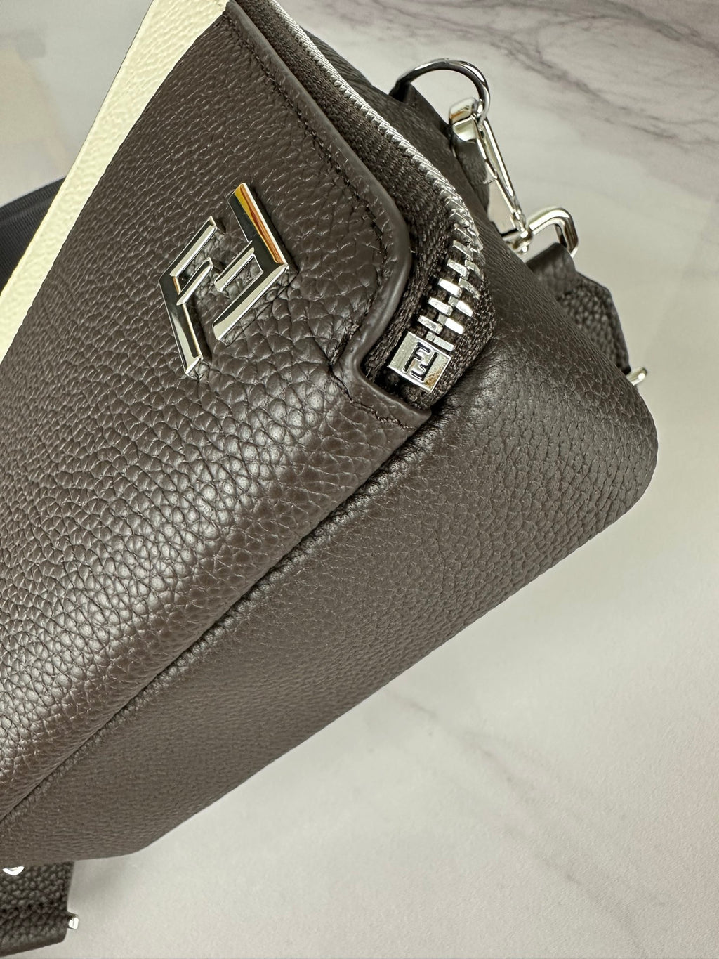 Fendi crossbody bag with engraved FF logo plate and silver zipper on textured dark leather.