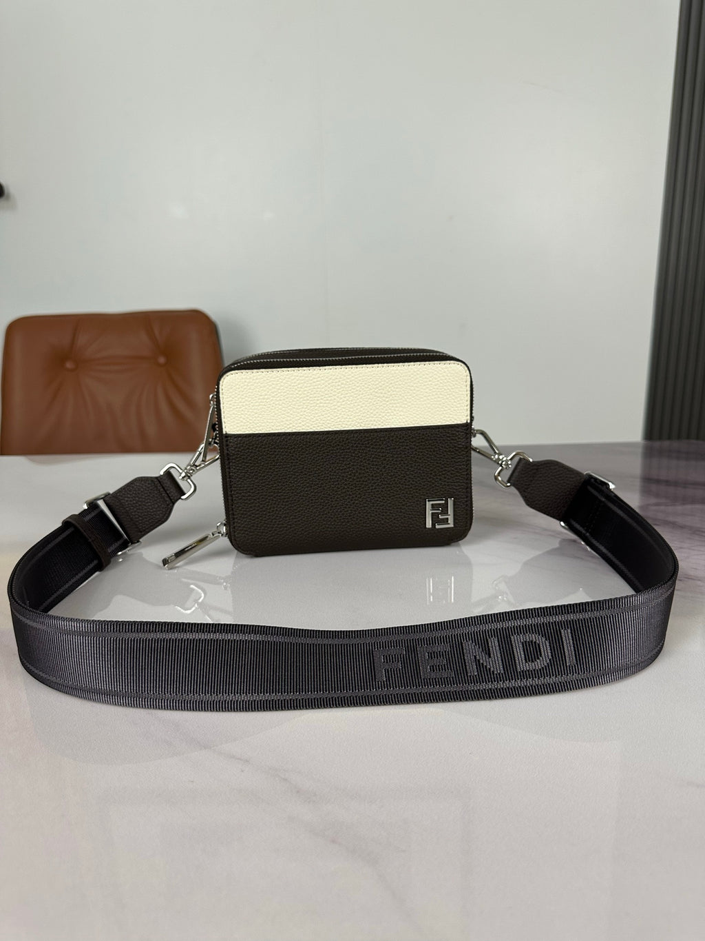 Fendi crossbody bag in dark and cream with logo buckle and adjustable strap.