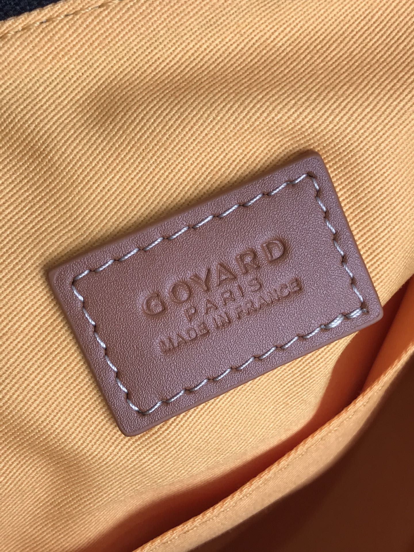 Leather brand patch tag with embossed text on tan fabric flap