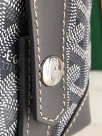 Goyard bag close-up: round metal emblem on dark leather tab with stitched edges