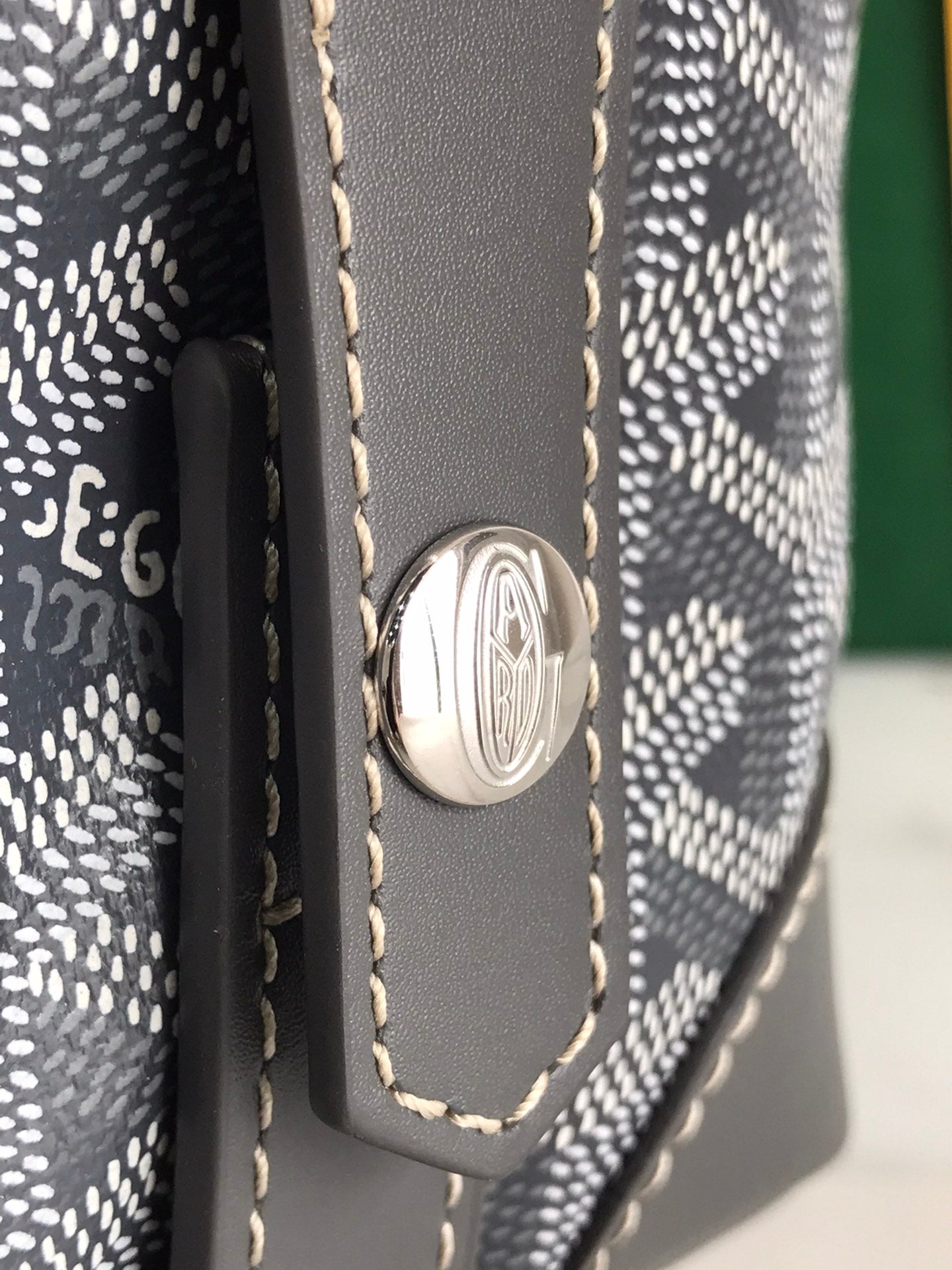Goyard bag close-up: round metal emblem on dark leather tab with stitched edges