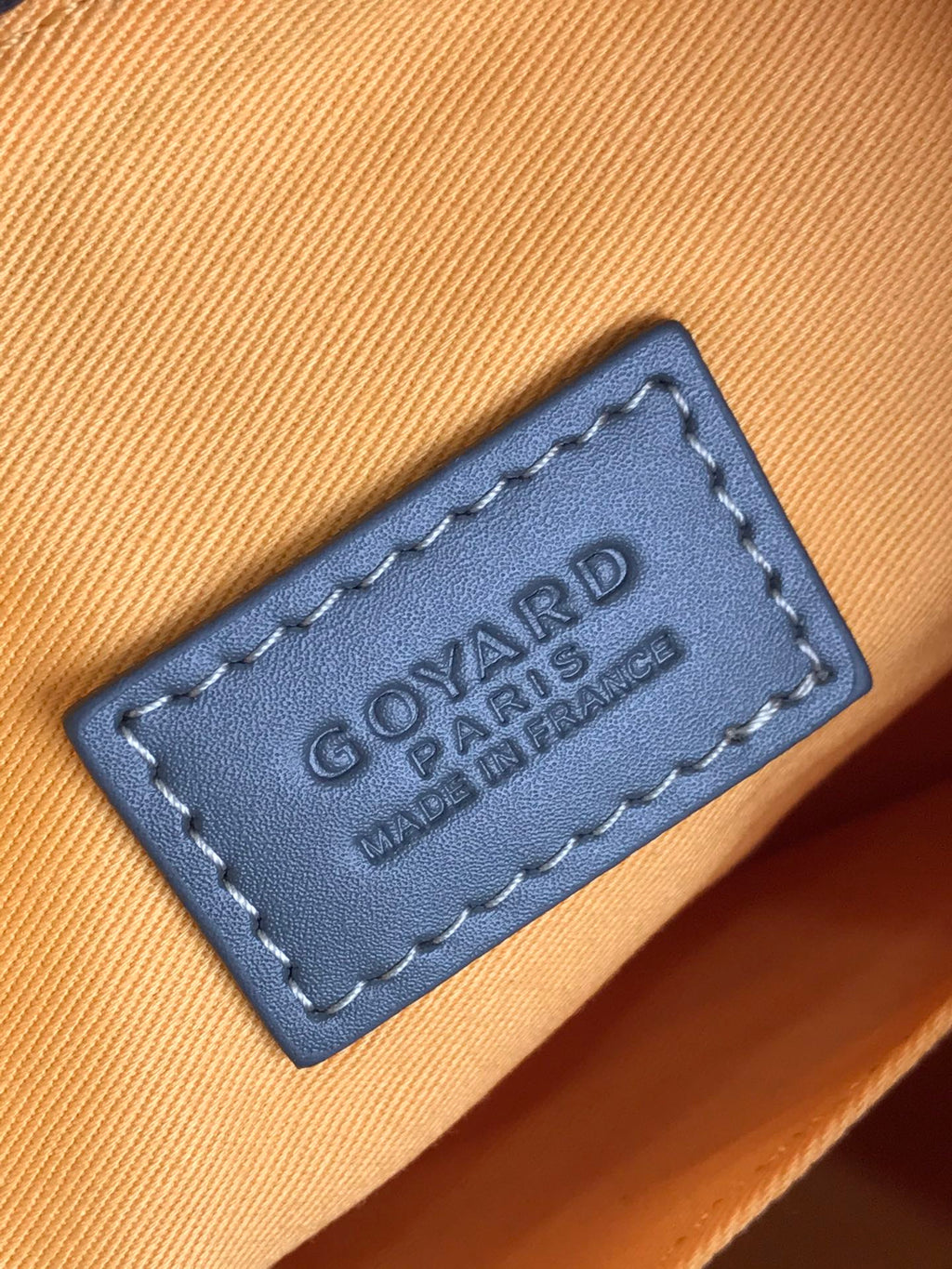Goyard bag leather brand patch reading “GOYARD PARIS” on tan fabric