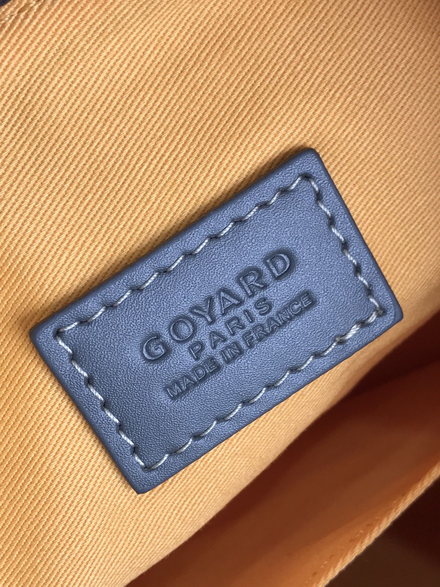 Goyard bag leather brand patch reading “GOYARD PARIS” on tan fabric