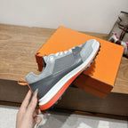 Grey low-top sneakers with white laces and orange rubber outsole edge