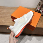 White sneaker held near orange shoebox with orange outsole trim