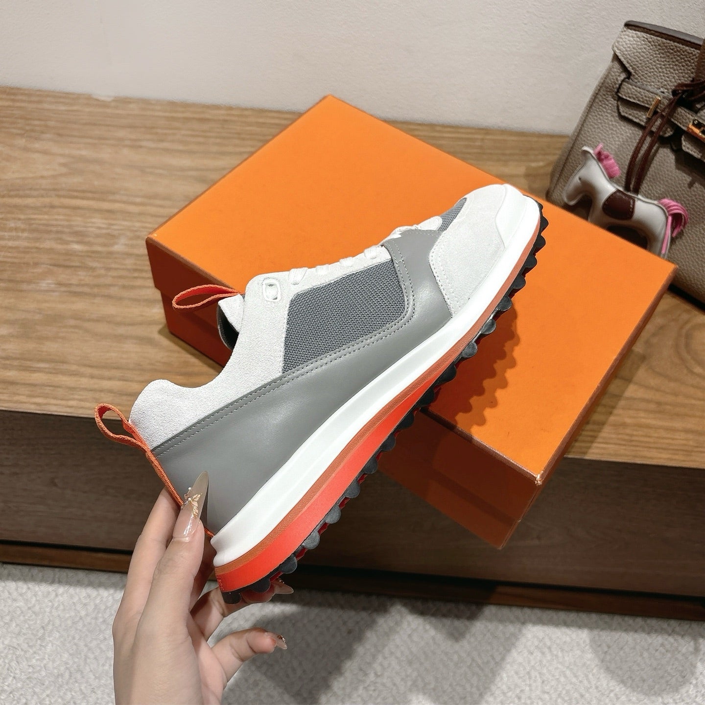 Hermes unisex sneakers in hand, white and gray uppers with orange edge detailing
