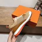 Hermes unisex sneaker held by hand, beige upper with brown panel and white sole with orange edge