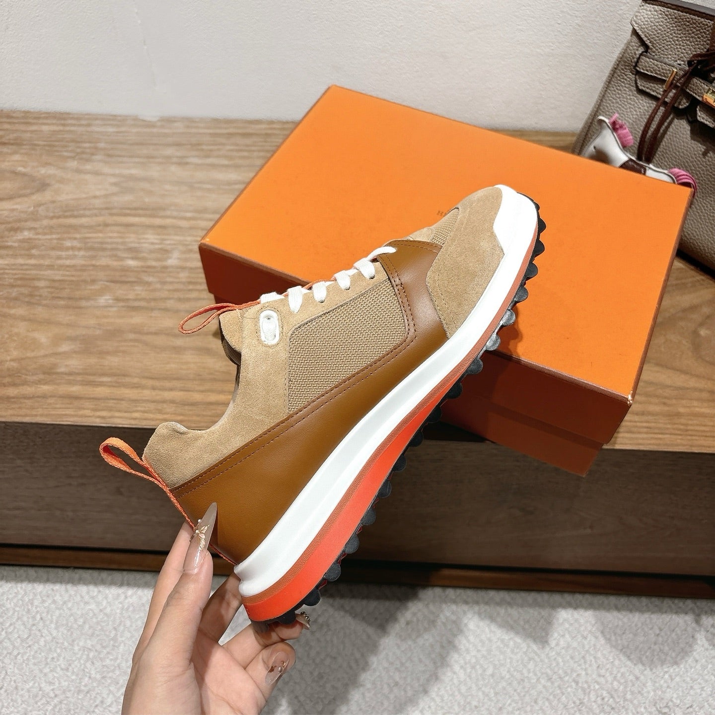 Beige Hermes sneakers with white laces, white midsoles, and orange outsole trim