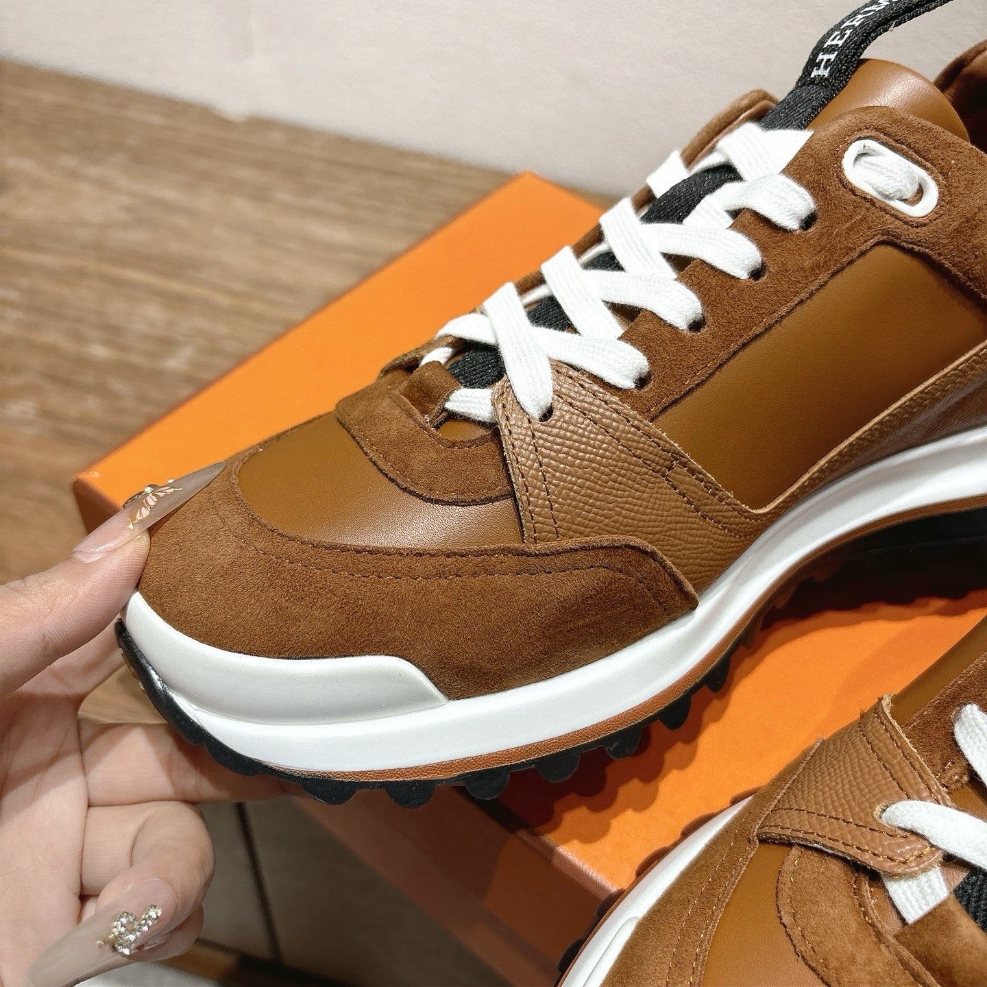 Brown Hermes unisex sneaker close-up with white laces, suede overlays, and sole
