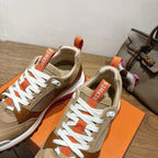 Hermes unisex sneaker close-up: white laces, beige upper, brown paneling, orange tag
