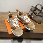 Pair of tan and brown Hermes sneakers with white laces and orange collar trim
