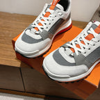 Hermes unisex sneakers, front view with white uppers, gray sides, orange-trim soles
