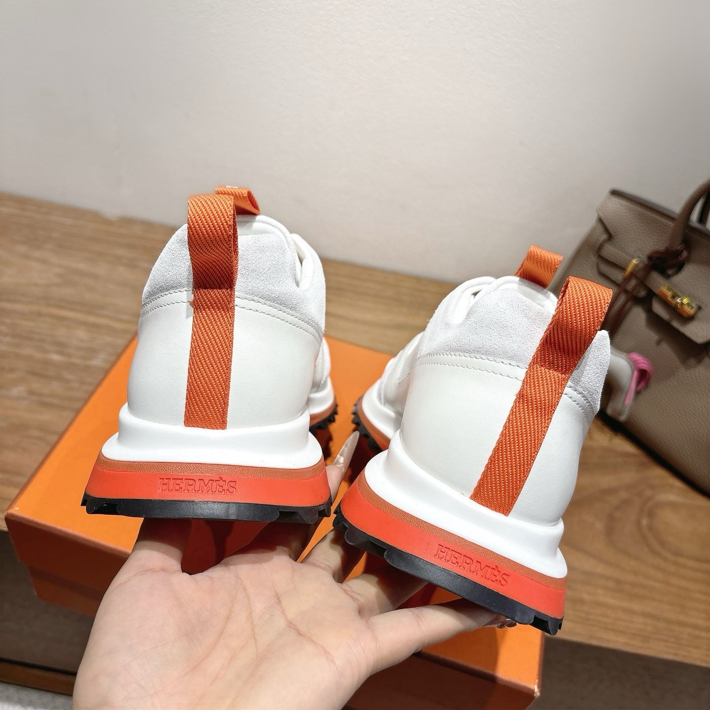 Back view of white sneakers with orange heel pull tabs on orange box