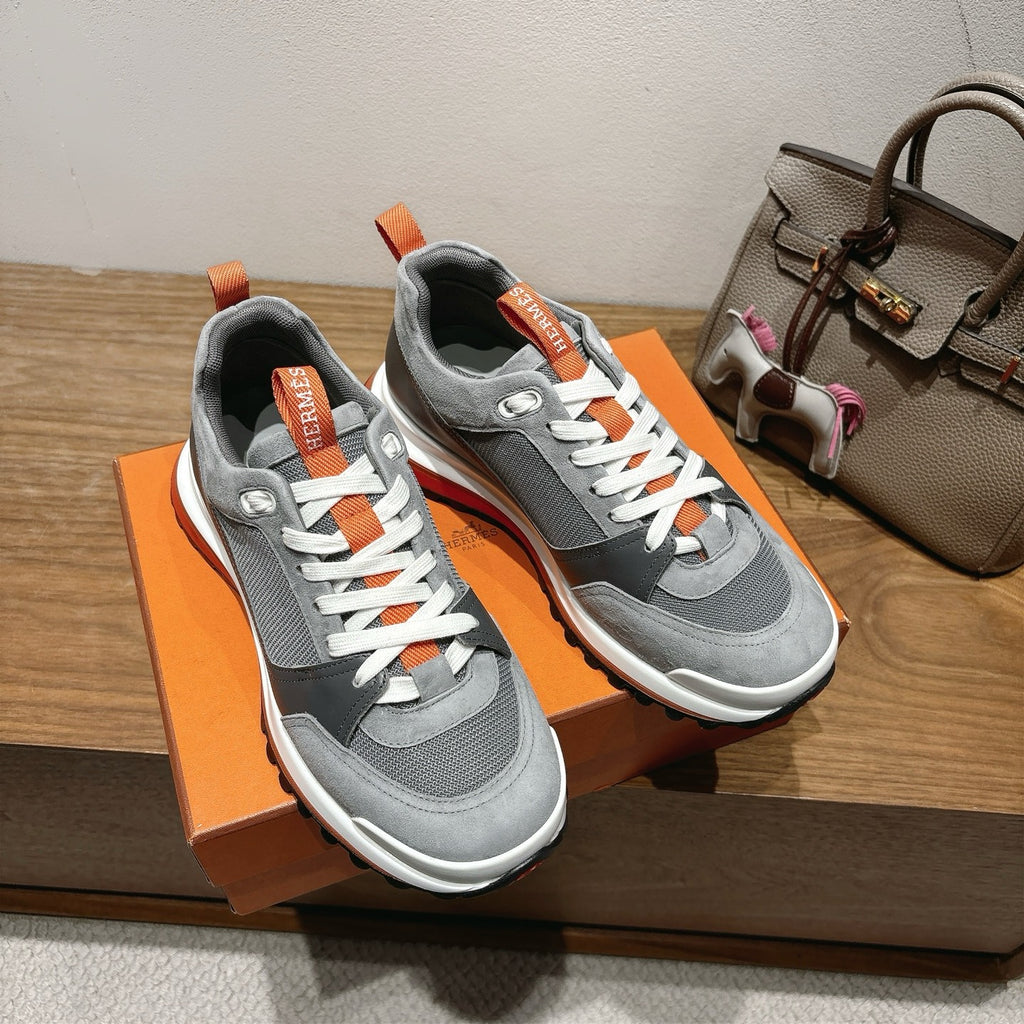 Pair of grey low-top sneakers with white laces, orange tag at tongue, orange trim