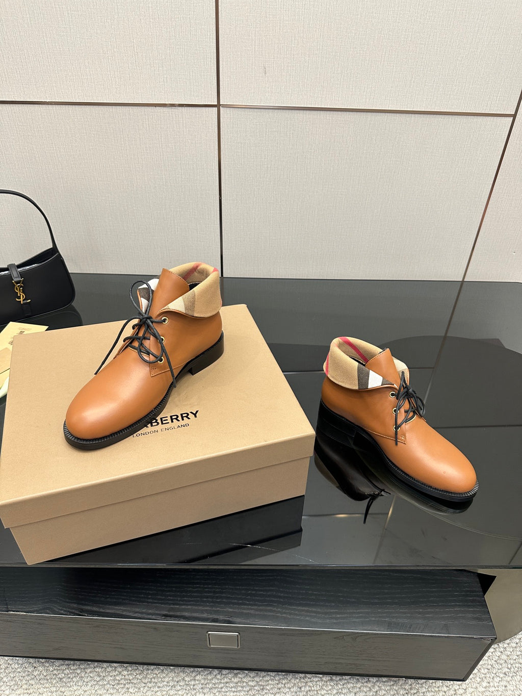 Two tan lace-up shoes on a box with black soles and plaid ankle trim